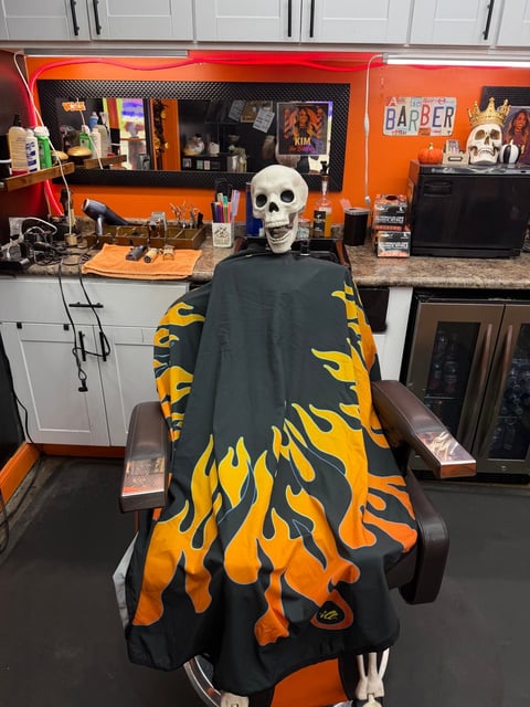 Skeleton mannequin wearing black cape with orange flame pattern in a barber shop setup with orange and black decor