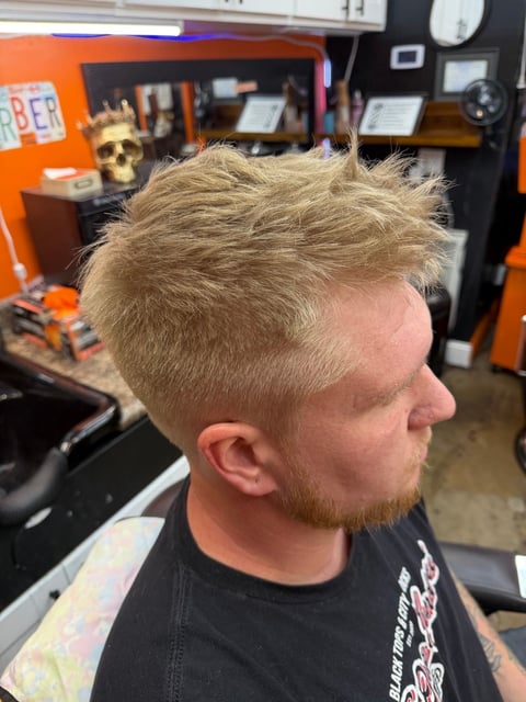 Side profile of man with short blonde textured haircut and beard in barber shop with orange and black interior