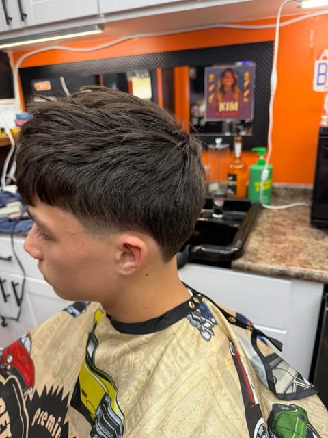 Profile view of a young person with a short dark layered haircut in a barbershop with orange and black decor