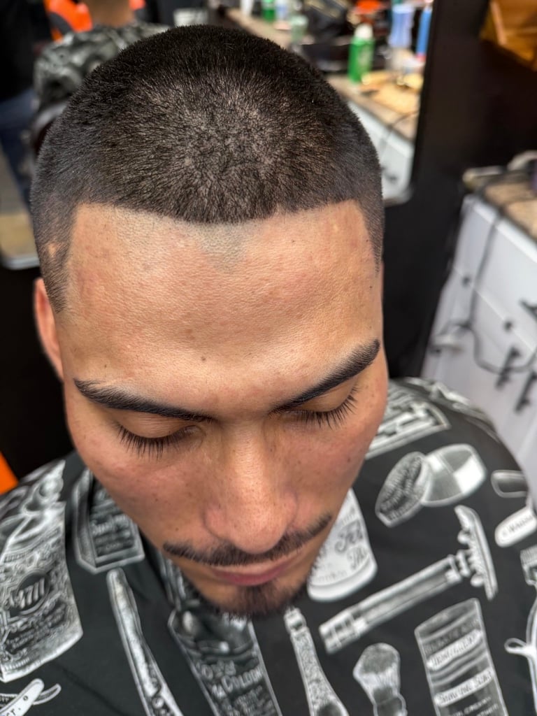 Man with a short buzzed haircut and facial hair, looking downward in a barbershop setting