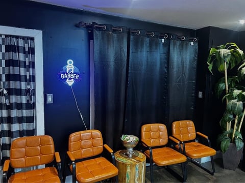 Modern barber shop interior with orange waiting chairs, neon barber sign, dark blue walls, and potted plants