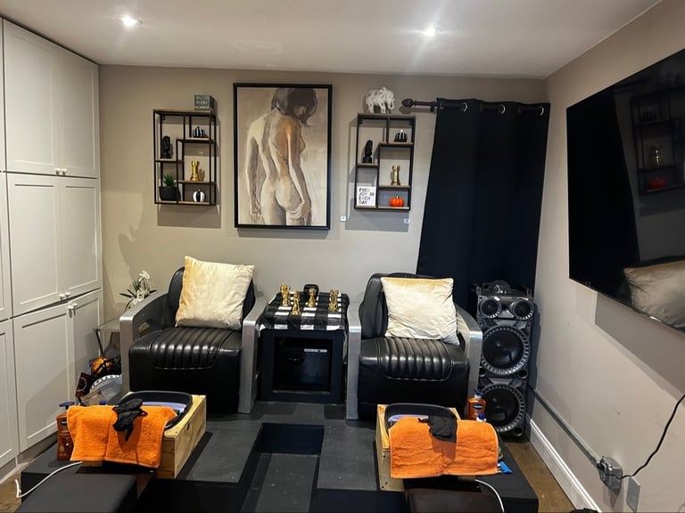 Modern home gym with black dumbbell rack, orange weights on mats, wall-mounted TV, and fitness decor on shelves