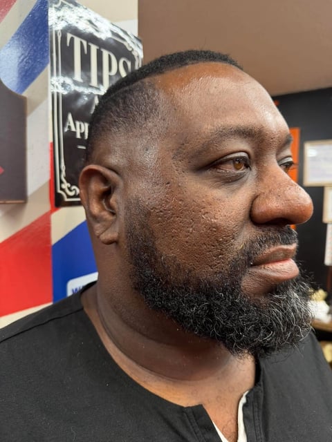 Portrait of a man with a beard wearing a black shirt, photographed in profile against a beer brand logo backdrop