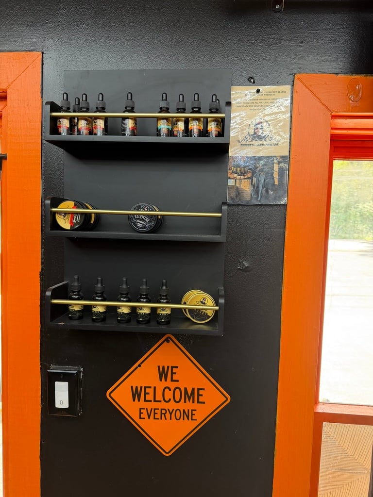 Black wall mounted pegboard organizer with orange handles, displaying tools, jars, and a We Welcome Everyone diamond sign